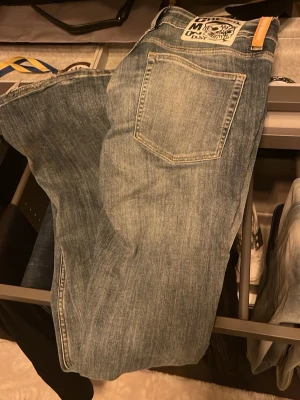 Blå slitna jeans med fransig kant - Säljer ett par blå jeans från weekday med coolt sliten look och fransiga benslut. Klassisk femficksmodell med en stor patch bak i midjan. Jeansen har en rak passform och är tillverkade i tåligt denimtyg. Perfekta för dig som gillar en avslappnad och edgy stil. Lite slitna längs nere se bild 2