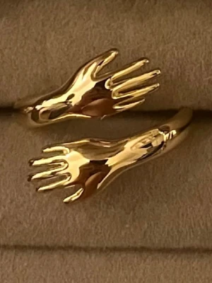 Ring -  smycke i form av en ring med två händer i guldton.