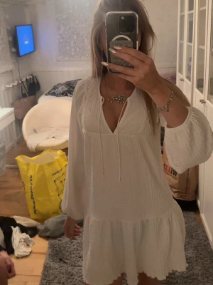 Vit kort klänning från Gina Tricot - Supersöt vit kort klänning från Gina Tricot i storlek XS. Klänningen har långa, luftiga ärmar, v-ringning med knytband och volangkant nertill. Materialet är strukturerat och känns lätt och bekvämt, perfekt för varma dagar.