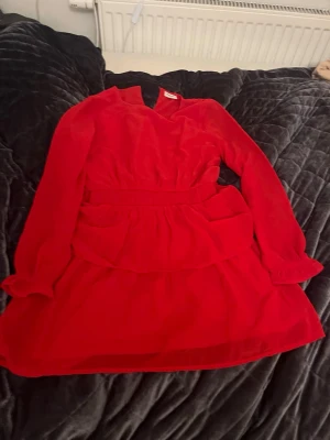 Röd volangklänning från Kappahl - Snygg röd kortklänning från Kappahl i storlek 152. Den har långa ärmar och volangdetaljer i kjolen.  Köpt för ca 300 kr, pris kan diskuteras. Funderingar? Skriv till mig💕
