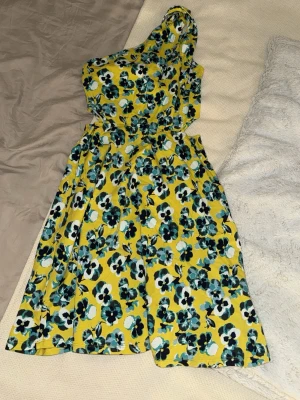 Gul blommig oneshoulder klänning - Säljer en superfin gul klänning med blåa blommönster. Perfekt för vår och sommar. 