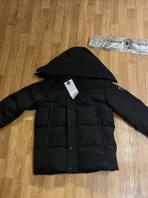 Svart pufferjacka från Canada Goose ÄKTA - Säljer min helt nya Canada Goose Black Label-puffer i svart, med tags och originalkvitto kvar. 	•	Storlek: S 	•	Färg: Svart 	•	Skick: Helt ny, aldrig använd 	•	Inkluderar: Originaltags och kvitto 	•	Nypris: ca 11000  Perfekt för dig som vill ha en äkta premiumjacka utan att betala fullpris i butik.  Snabb affär möjlig – prisförslag är välkommet! 