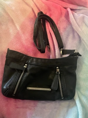 Svart axelväska från Björn Borg - Snygg svart axelväska från Björn Borg i skinnimitation. Väskan har två dragkedjefickor framtill, justerbar axelrem och ett stort huvudfack med dragkedja. Perfekt storlek för det viktigaste och stilren metallbricka med logga på framsidan.