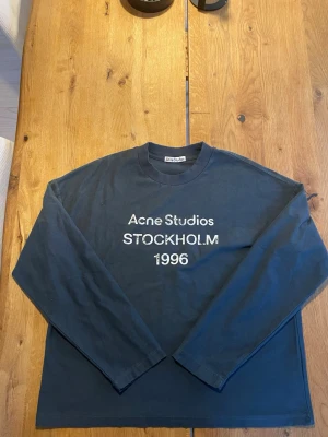 Mörkblå långärmad t-shirt Acne Studios - Snygg mörkblå långärmad t-shirt från Acne Studios med tryck 'STOCKHOLM 1996' på bröstet. Klassisk rund halsringning och relaxed fit. Perfekt för dig som gillar stilrena plagg med en urban touch. Storlek S ny skick 