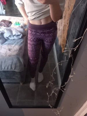 Lila leggings med vintermönster - Säljer ett par lila leggings i storlek S med snyggt vinterinspirerat mönster i olika nyanser av lila och vitt. De är högmidjade och sitter tight, perfekta för chill dagar eller som mysbyxor. Materialet är mjukt och stretchigt, 98% polyester och 2% elastan.