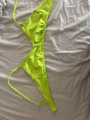Neongul bikiniöverdel med smala band - Säljer en neongul bikiniöverdel med trekantsform och smala axelband. Bikinin har enkel design utan mönster och är fodrad på insidan. Perfekt för dig som vill sticka ut på stranden.