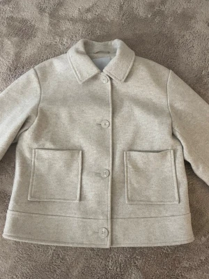 Beige ulljacka från 157 - Säljer en stilren beige jacka från 157 i ullmix. Jackan har klassisk krage, stora framfickor och stängs med knappar framtill. Perfekt för dig som gillar minimalistisk och clean look. Passar till både jeans och kjol. Har aldrig använt nypris 300kr tar gärna emot bud och skriv om ni har frågor💕😊