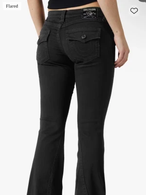Svarta bootcut jeans från true religion  - Säljer ett par svarta flared jeans från True Religion med snygga ficklock och dekorativa sömmar bak. Byxorna har normal midja och klassisk bootcut passform som ger en schysst siluett. Perfekta till sneakers eller boots.