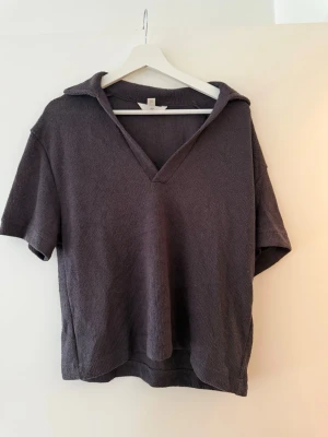 Mörkgrå stickad tröja från H&M - Säljer en mörkgrå stickad tröja från H&M med korta ärmar och v-ringad krage. Toppen har en avslappnad passform och är gjord i mjukt stickat material, perfekt för en chill och stilren look.