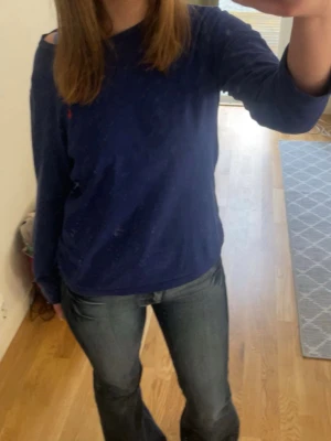 Blå långärmad tröja från Polo Ralph Lauren - Snygg marinblå långärmad tröja från Polo Ralph Lauren med klassisk rund hals och röd broderad logga på bröstet. Tillverkad i mjuk bomull, perfekt för chill dagar. Enkel och stilren design som funkar till jeans eller shorts.