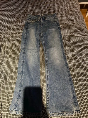 Blå bootcut jeans från Gina Tricot short  - Säljer ett par klassiska blå jeans från Gina Tricot med bootcut passform. Jeansen har normal midja, fem fickor och snygga slitningar framtill. Tillverkade i mjukt denimtyg som sitter skönt hela dagen.