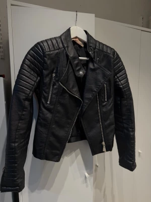 Skinnjacka - Cool svart bikerjacka från chiquelle i skinnimitation med quiltade detaljer på axlar och ärmar. Jackan har snedställd dragkedja, två dragkedjefickor framtill och markerad krage. Perfekt för en edgy streetstil. Pris kan diskuteras.