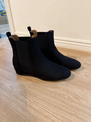 Svarta boots  - Säljer ett par klassiska svarta chelsea boots från Anna field i mjuk mocka. Skorna har rund tå, låg klack och elastiska paneler på sidorna för enkel påtagning. Perfekta till jeans eller kjol för en clean look.