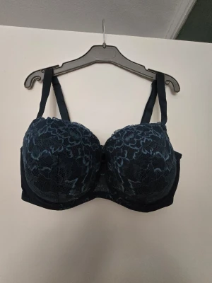 Blommig spets-bh från Lindex  - Snygg svart bh från Lindex med blommigt spetsmönster och vadderade kupor. Axelbanden är justerbara och bh:n har en elegant look med fina spetsdetaljer. Perfekt för dig som vill ha något både bekvämt och stilrent.