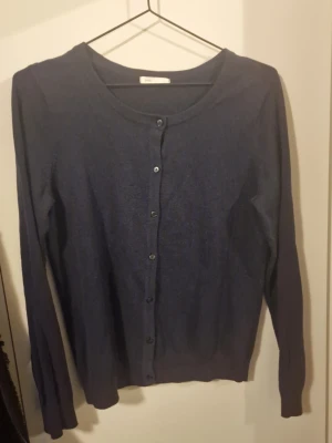 Mörkblå kofta med knappar - En enkel och stilren mörkblå kofta från Basic. Koftan har rund halsringning, långa ärmar och knäppning med små knappar framtill. Perfekt att slänga över en t-shirt eller linne för en chill look.