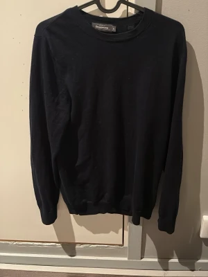 Mörkblå merinoulltröja från Dressmann - Klassisk marinblå tröja från Dressmann i mjuk merinoull. Enkel rund halsringning och långa ärmar, perfekt för lager på lager under vår och vinter. Snygg och stilren modell som passar till det mesta. Storlek M.