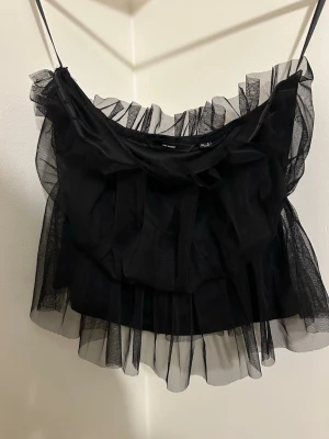 Svart volangig tubtopp från Vero Moda - Säljer en svart tubtopp från Vero Moda med flera lager av transparent volangig mesh. Toppen har en bandeauform och är axelbandslös.