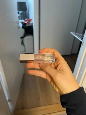 Fenty Beauty Gloss Bomb Glass Slipper - Gloss Bomb Universal Lip Luminizer ger explosiv glans och finns i flera universella nyanser som handplockats av Rihanna själv för att fungera som den ultimata finishen till varje look. Ett läckert svep med Gloss Boms XXL-applikator ger läpparna mer att älska, medan mjukgörande sheasmör vårdar inifrån. Gloss Bomb får läpparna att omedelbar