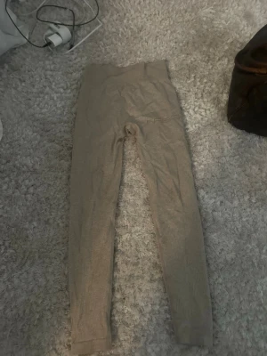 Beige ribbade träningstights  - Säljer ett par beige ribbade träningstights. De har hög midja och är tillverkade i ett stretchigt material som sitter tight och bekvämt. Perfekta för träning eller chill dagar. Diskret logga på höften och mjuk känsla.