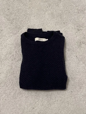 Lacrosse tröja - Säljer en mörkblå stickad tröja från Lacrosse Premium Line i storlek S. Tröjan har ett diskret strukturmönster, rund halsringning och ribbade muddar. Materialet är 55% extrafin merinoull och 45% bomull, vilket gör den både mjuk och varm.