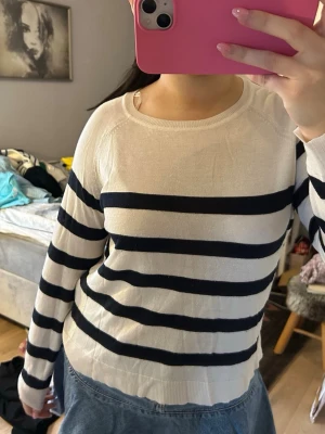 Randig vit och marinblå tröja - Säljer en vit tröja med breda marinblå ränder. Tröjan har rund halsringning och långa ärmar. Den är tunn och mjuk, perfekt för lager-på-lager. Passformen är normal och materialet känns som bomull eller en bomullsblandning.