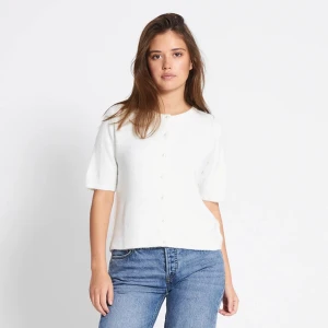 Vit kofta med pärlknappar från 157 - Superfin vit kofta från 157 med kort ärm och rund hals. Koftan har pärlknappar framtill och är stickad i ett mjukt material. 