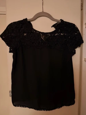 Svart blus med spetsdetaljer - Säljer en svart blus från Mango. Blusen har rund halsringning och en liten knapp i nacken. 