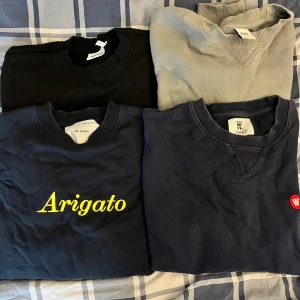 Svart sweatshirt Weekday, blå Axel Arigato, woodwood och Zara  - Mörkblå sweatshirt från Axel Arigato med gul text 'Arigato' på bröstet. Klassisk rund halsringning och ribbade muddar. Perfekt för dig som gillar stilrena och trendiga plagg.  150:-/st för Arigato och woodwood, 80:-/st för Weekday och Zara. Hela och rena, finns vid Mariatorget 