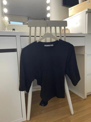 Svart croppad topp från 157 - Svart croppad topp från 157 med rund halsringning och trekvartsärm. Toppen har en snygg knytning bak i midjan som ger en cool detalj. Tillverkad i mjuk bomull som känns skön mot huden. Perfekt till jeans eller kjol för en enkel men trendig look.