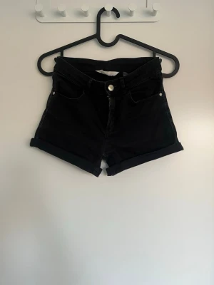 Svarta high waist shorts från H&M - Säljer ett par svarta high waist shorts från H&M. Klassisk femficksmodell med uppvikta benslut och knapp- samt dragkedjestängning. Perfekta till sommaren och lätta att matcha med allt. Materialet är mjuk bomull med lite stretch.