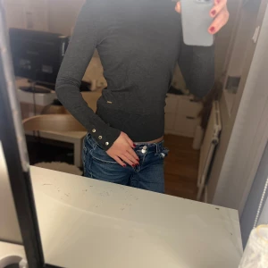Mörkgrå långärmad tröja med knappar - Säljer en stilren mörkgrå tröja i mycket bra skick. Endast använd 2 gånger! Den är långärmad och har snygga knappar vid ärmsluten.  Tröjan är tight och framhäver figuren på ett snyggt sätt. Säljer då den inte används så mycket! 
