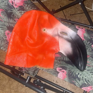 Flamingoformad mask - Cool flamingoformad mask i stark orange och svart. Perfekt för maskerad eller fest! Den är gjord av ett flexibelt material som formar sig efter huvudet. Masken har detaljerade drag och en stor näbb som verkligen sticker ut.