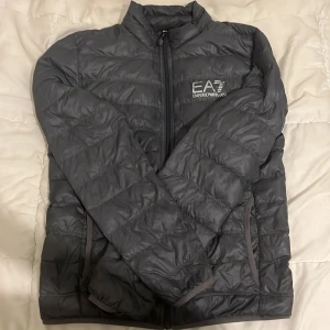 EA7 jacka - Säljer min armani jacka som jag har haft i några månader pga använder inte den längre den är i bra skick men som ni ser i sista bilden har den två små skador bakifrån.köpte den för 1500 kr,storlek (S) skriv om ni är intresserade 😁