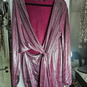 Glittrig rosa omlottklänning - Superfin glittrig rosa omlottklänning i storlek XL som bra kan beskrivas som disco. Klänningen har långa ärmar och sitter omlott framtill, går att justera genom att dra. Perfekt för festliga tillfällen när du vill glänsa lite extra! ✨ Endast använd en gång, inga defekter. 