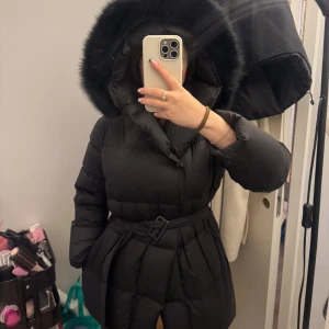 Vinterjacka i dun  - Superfin och tidslös vinterjacka i svart. Använt under en vintersäsong. Jackan har inga defekter, den har knappar både nere och uppe, samt bälte som medföljer. Den är i dun så den kommer hålla dig varm på vintern. Nypris cirka 4000kr