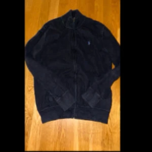 Marinblå ralph lauren kofta - Säljer en mysig marinblå kofta  i mycket bra skick. Perfekt för kyliga höst- och vinterdagar. Koftan  har en dragkedja framtill och långa ärmar. Den är både stilren och bekväm, idealisk för vardagsbruk eller en avslappnad utflykt.