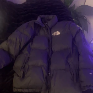 Svart dunjacka från The North Face - Säljer en svart dunjacka från The North Face i mycket bra skick. Jackan är perfekt för kalla vinterdagar och har en bekväm passform. Den har en dragkedja framtill och är långärmad. Perfekt för dig som vill hålla värmen med stil!
