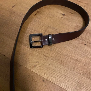 Brunt skärp med silverfärgat spänne - Säljer ett stilrent brunt skärp i skinn med ett klassiskt silverfärgat spänne. Perfekt för både vardag och fest. Skärpet är i bra skick och passar de flesta outfits. Ett måste i garderoben för den som gillar tidlös stil!