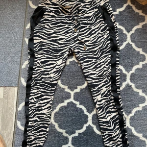 Zebramönstrade byxor från FAV - Säljer ett par coola zebramönstrade byxor från FAV. De har en bekväm passform med snörning i midjan och svarta sidopaneler som ger en snygg kontrast. Perfekta för en avslappnad stil eller en utekväll. 🦓✨