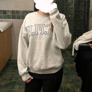 Säljer en grå sweatshirt från Gina Tricot i storlek S. Den har trycket 'SCFLH' i mörkblått på framsidan. Tröjan är perfekt för en avslappnad stil och har långa ärmar med ribbade muddar. Superbekväm och lätt att matcha med jeans eller leggings! Tröjan är använd och därmed tvättad så den är inte precis lika mjuk som originalet men fortfarande otrolig!