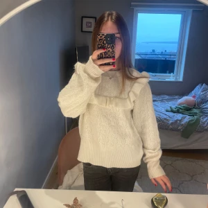 Vit stickad tröja med volangdetaljer - Superfin vit stickad tröja med volangdetaljer på bröstet. Passar perfekt till både vardag och festliga tillfällen!