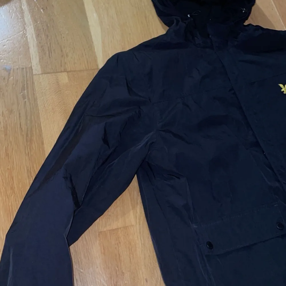 Säljer en snygg svart jacka från Lyle & Scott i storlek S. Den har en huva och är långärmad, perfekt för höst och vår. Jackan har en dragkedja och samt en liten gul logga på bröstet. Den är i mycket bra skick och passar till vardag. Jackor.