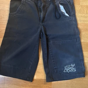Jorts - Säljer ett par svarta jorts från Dope'n Science i mycket bra skick. De har en cool graffiti-liknande logga på benet och en broderad detalj på bakfickan. Perfekta för en avslappnad stil med elastisk midja och dragkedja. Passar bra till sommarens alla äventyr!