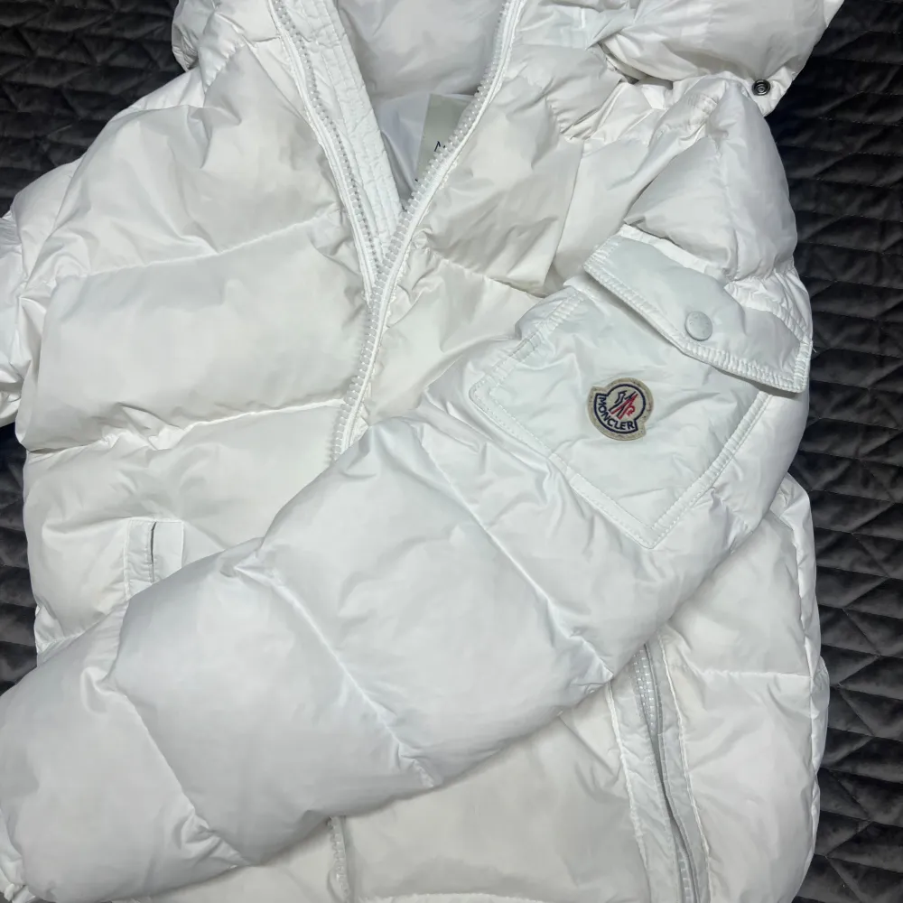 Säljer en snygg vit dunjacka från Moncler i mycket bra skick. Jackan har en dragkedja framtill och en mysig huva för extra värme. Perfekt för kalla vinterdagar! Den är quiltad och har en stilren design som passar till det mesta. 👍. Takit.