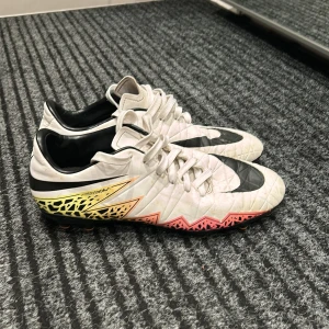 Nike fotbollsskor i vitt och svart - Säljer ett par coola Nike fotbollsskor i vitt med svarta detaljer och en färgglad sula. Skorna har snörning och är i bra skick. Perfekta för fotbollsträningen eller matchen. Storlek herr 42. Passa på att köpa dessa grymma skor!