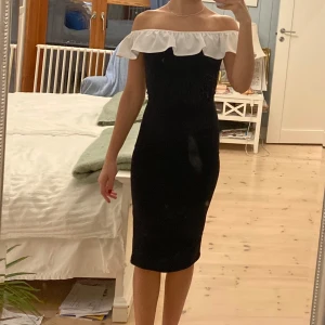 Svart offshoulder klänning med volang - Snygg svart offshoulder klänning med vit volangdetalj runt axlarna. Sitter jättesnyggt på. Aldrig använd, endast provad. 