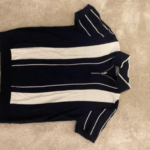 Blå och vit pikétröja från Primark - Säljer en snygg blå och vit pikétröja från Primark i storlek M. Tröjan har korta ärmar och en dragkedja vid halsen. Perfekt för en avslappnad stil eller en dag på stan. Den är i mycket bra skick och redo för nya äventyr!