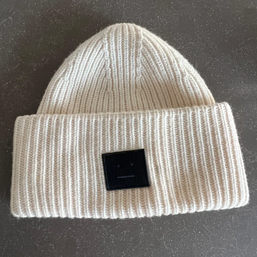 Säljer en superfin beige stickad mössa från Acne Studios. Den är ribbad och har en svart patch framtill som ger en cool touch. Perfekt för att hålla sig varm under höst och vinter. Mössan är i bra. skick och passar de flesta tack vare sin stretchiga design. Har lite sminkfläckar på insidan! . Accessoarer.