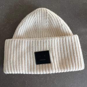 Säljer en superfin beige stickad mössa från Acne Studios. Den är ribbad och har en svart patch framtill som ger en cool touch. Perfekt för att hålla sig varm under höst och vinter. Mössan är i bra. skick och passar de flesta tack vare sin stretchiga design. Har lite sminkfläckar på insidan! 