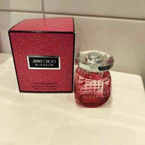 Jimmy Choo Blossom Eau de Parfum - Säljer en Jimmy Choo Blossom Eau de Parfum. Flaskan är rosa med en elegant, glittrande yta och ett genomskinligt lock. Doften är blommig och fruktig, perfekt för att ge en fräsch känsla. Förpackningen är också rosa med glitterdetaljer.
